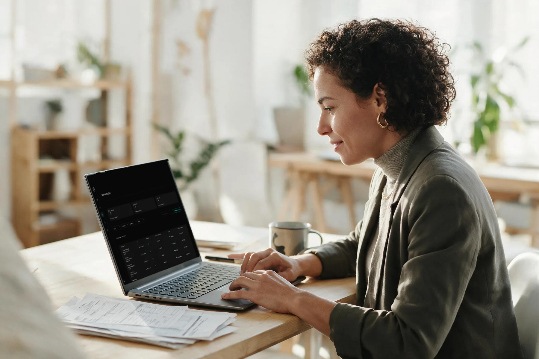 Uma analista de benefícios trabalha concentrada num escritório claro, com o painel de movimentações do Portal RH aberto no notebook e formulários impressos ao lado.