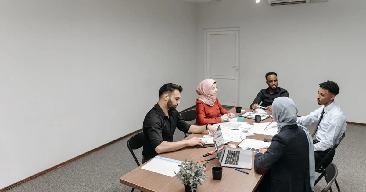 Grupo reunido em torno de uma mesa de reunião com documentos impressos, planilhas e notebook aberto