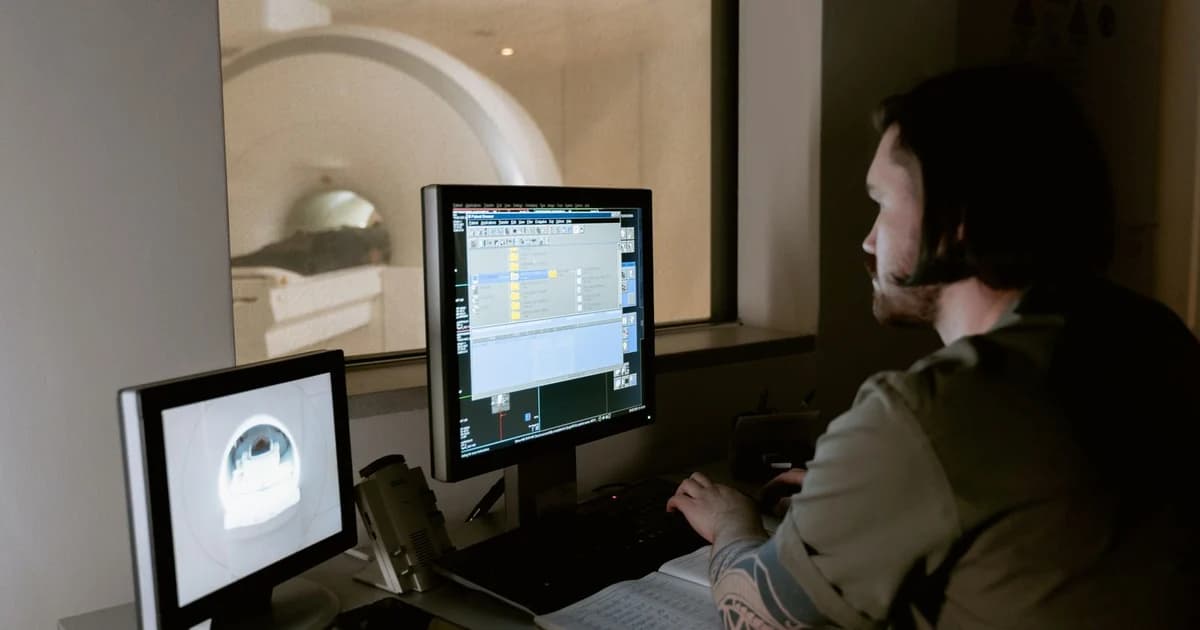 Profissional de saúde de costas observando monitor com imagens de ressonância magnética em sala de exame com pouca luz