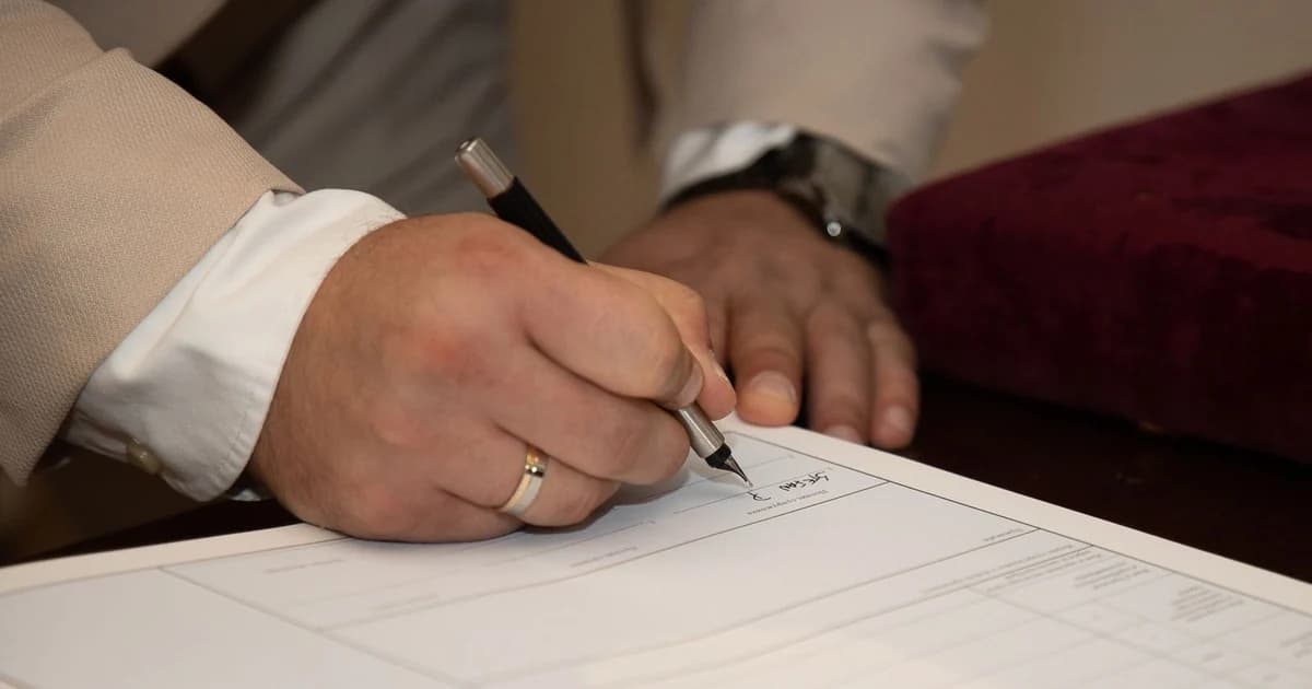 Mão assinando um documento contratual sobre a mesa, em close
