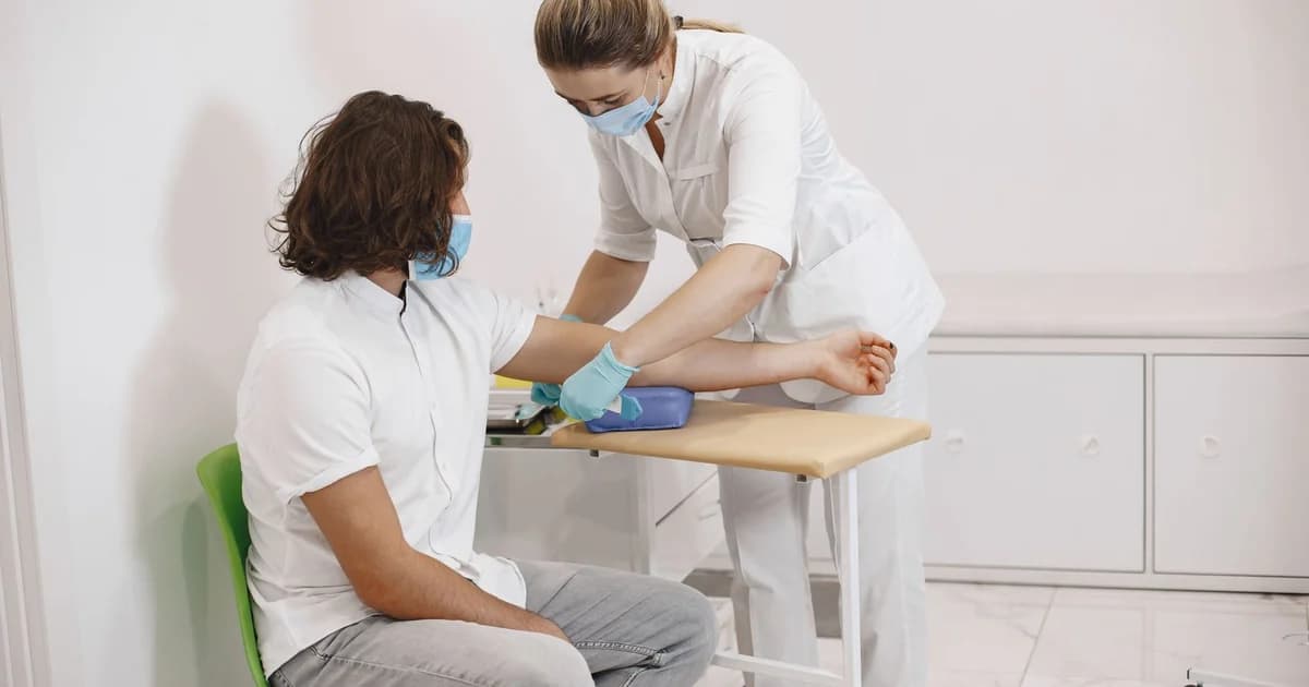 Trabalhador adulto sentado durante coleta de exame ocupacional, com profissional de saúde de jaleco branco ao lado, em sala clínica clara