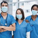 Uma fotografia, um grupo de 3 enfermeiros, sendo 1 homem e 2 mulheres, o homem está ao lado esquerdo da imagem, seguindo com as duas mulheres ao lado.